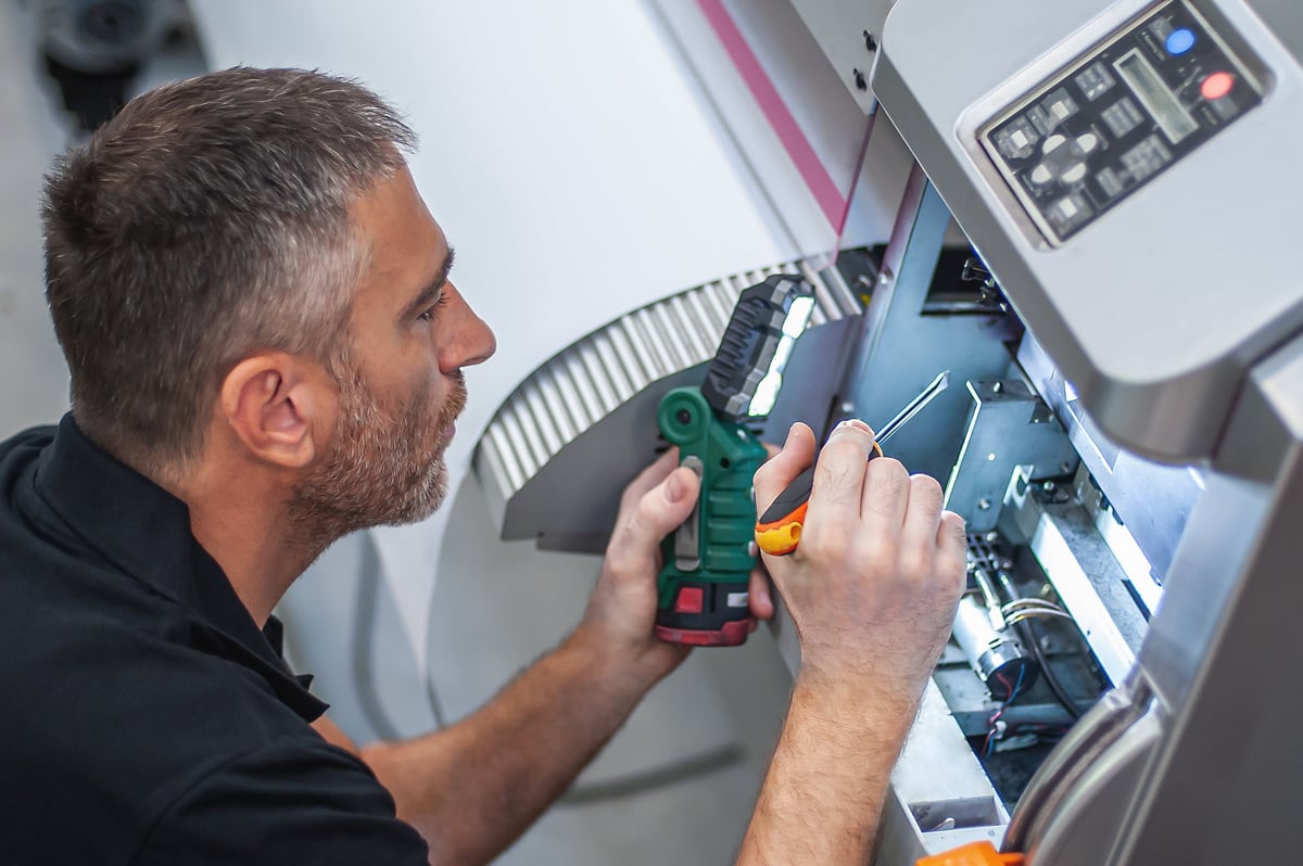 Técnico profesional reparando y dando mantenimiento a impresora industrial en taller de impresión