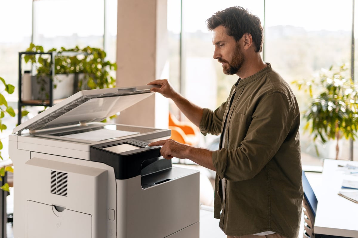 Oficinista operando una impresora multifuncional en una oficina moderna con plantas y luz natural